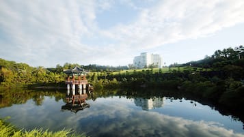 A serene lake with a traditional pavilion and a modern building in the background.