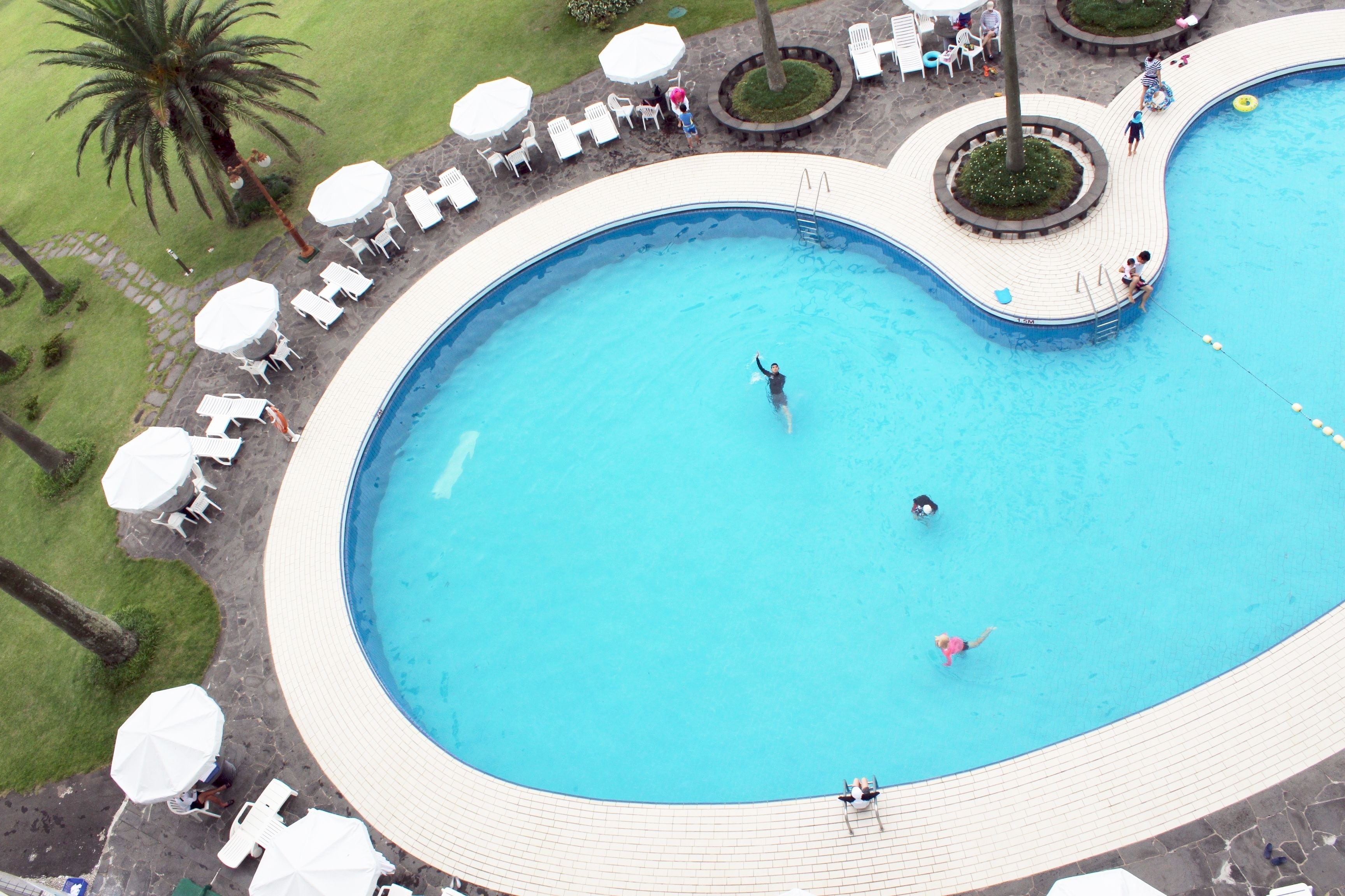 An aerial view of a swimming pool with a curved edge, surrounded by white lounge chairs and umbrellas.