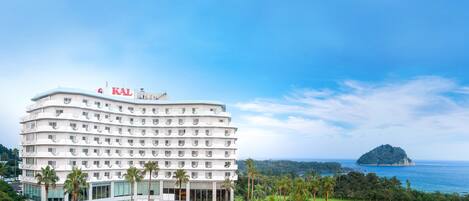 Un hotel de varios pisos con zona de piscina, rodeado de exuberante vegetación y vistas al océano.