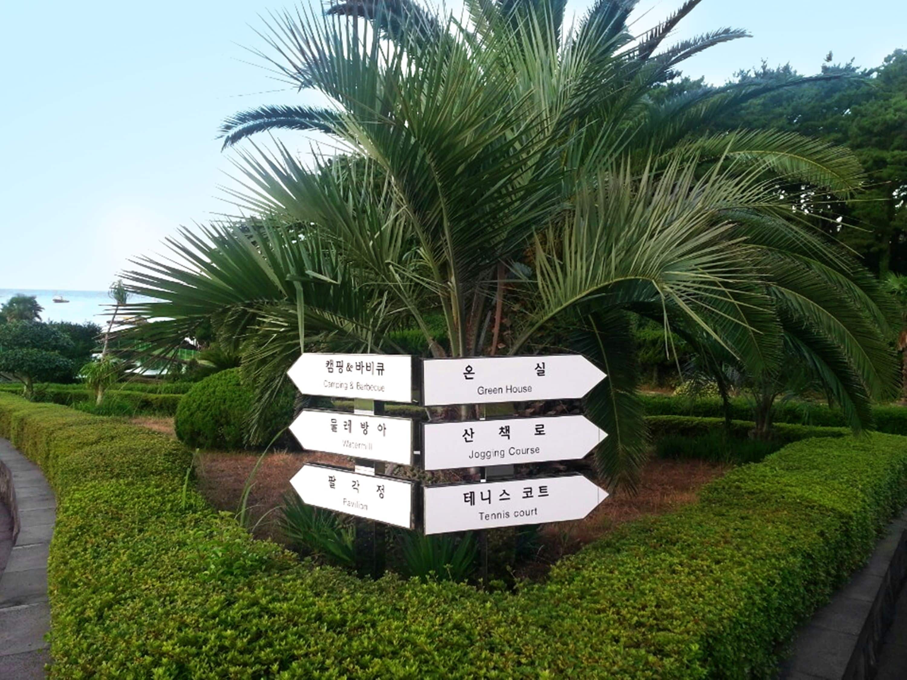 A directional signpost with multiple arrows pointing to various facilities such as a Green House, Jogging Course, Pavilion, and Tennis Court.