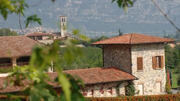 Un edificio in pietra con tetto in tegole, immerso nel verde con una montagna sullo sfondo.