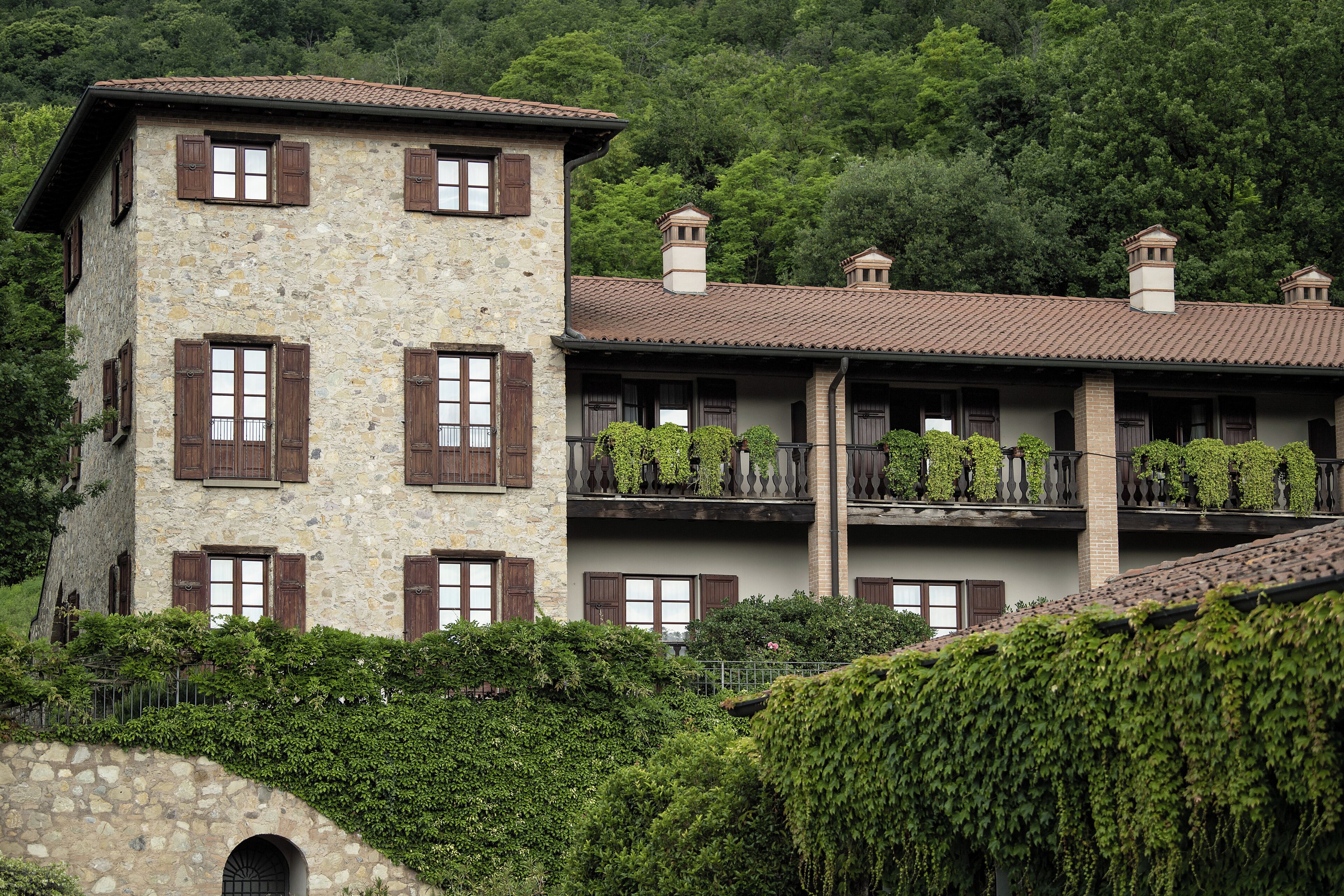 A stone building with multiple windows and balconies, surrounded by lush greenery.