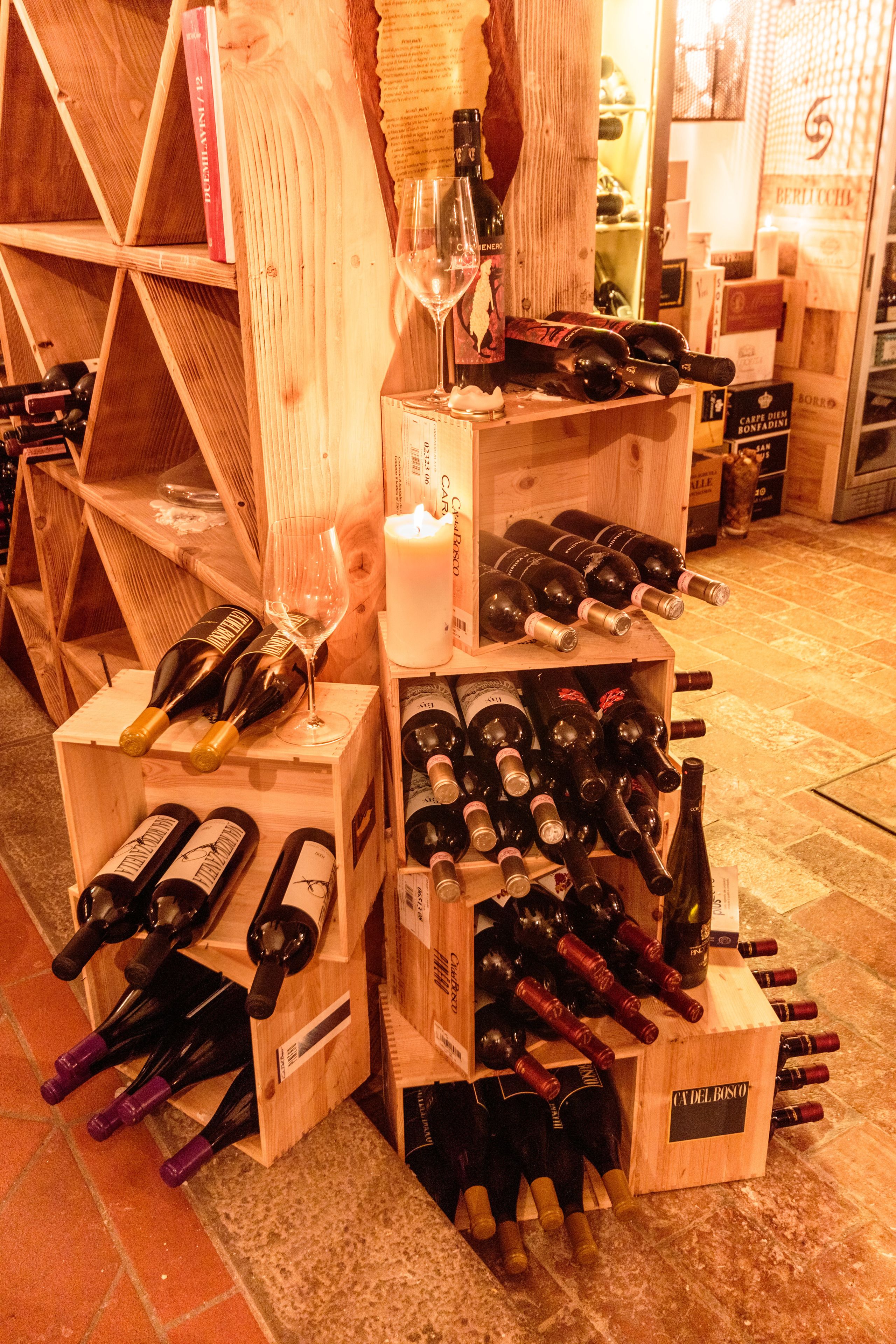 A wine cellar with wooden crates containing various bottles of wine, a candle, and a wine glass.