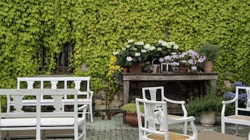 Un espace patio avec des chaises blanches, une table agrémentée de plantes en pot et un mur recouvert de lierre vert.