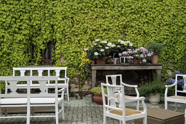 A patio area with white chairs, a table with potted plants, and a wall covered in green ivy.