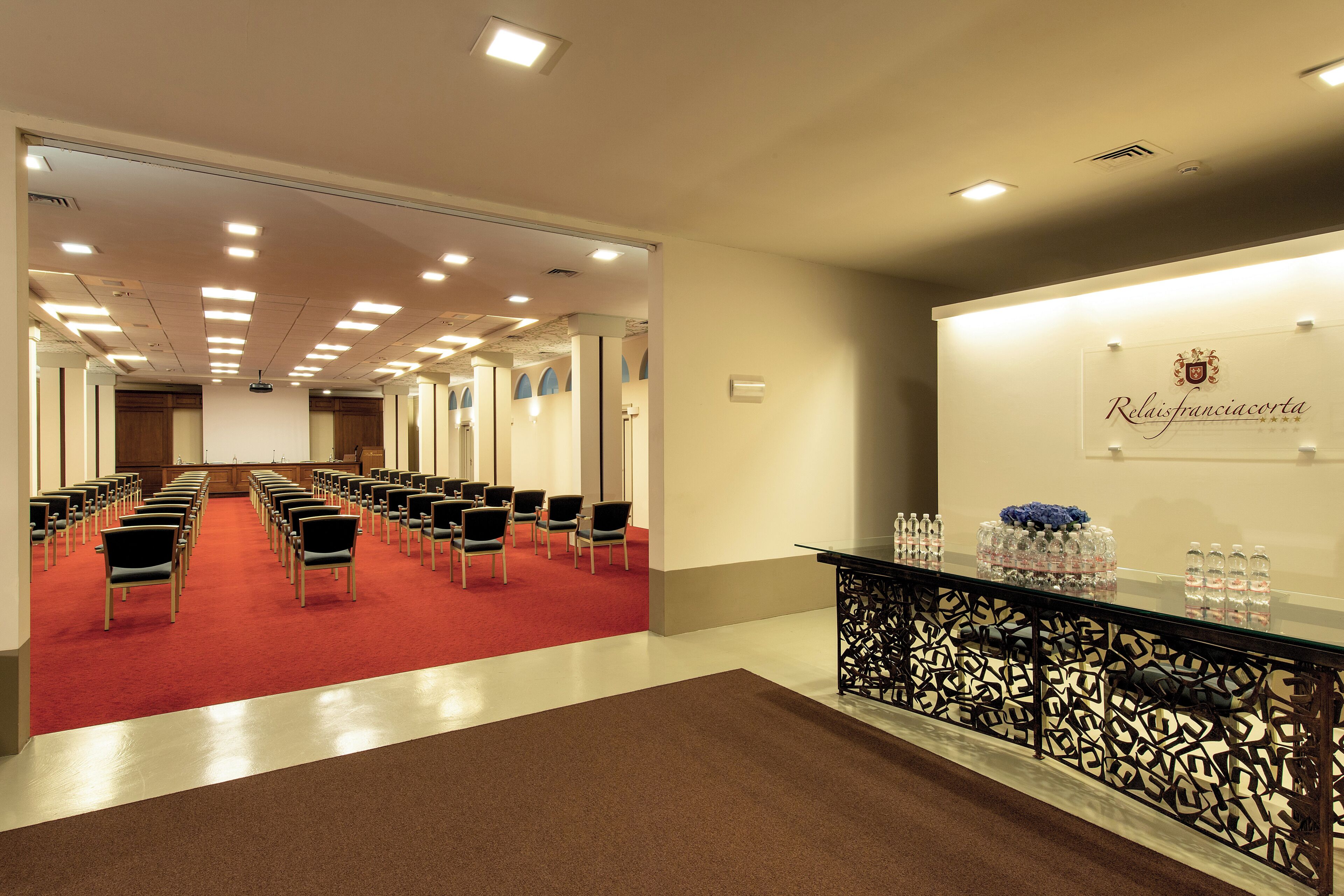 Een hotel lobby met rijen stoelen, een receptiebalie en een gebied met een rode tapijtvloer.