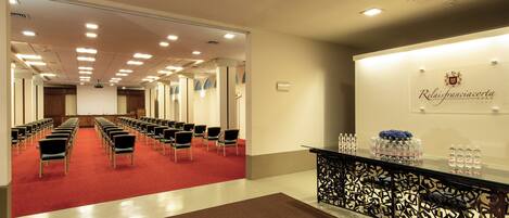 A hotel lobby with rows of chairs, a reception desk, and a red carpeted area.