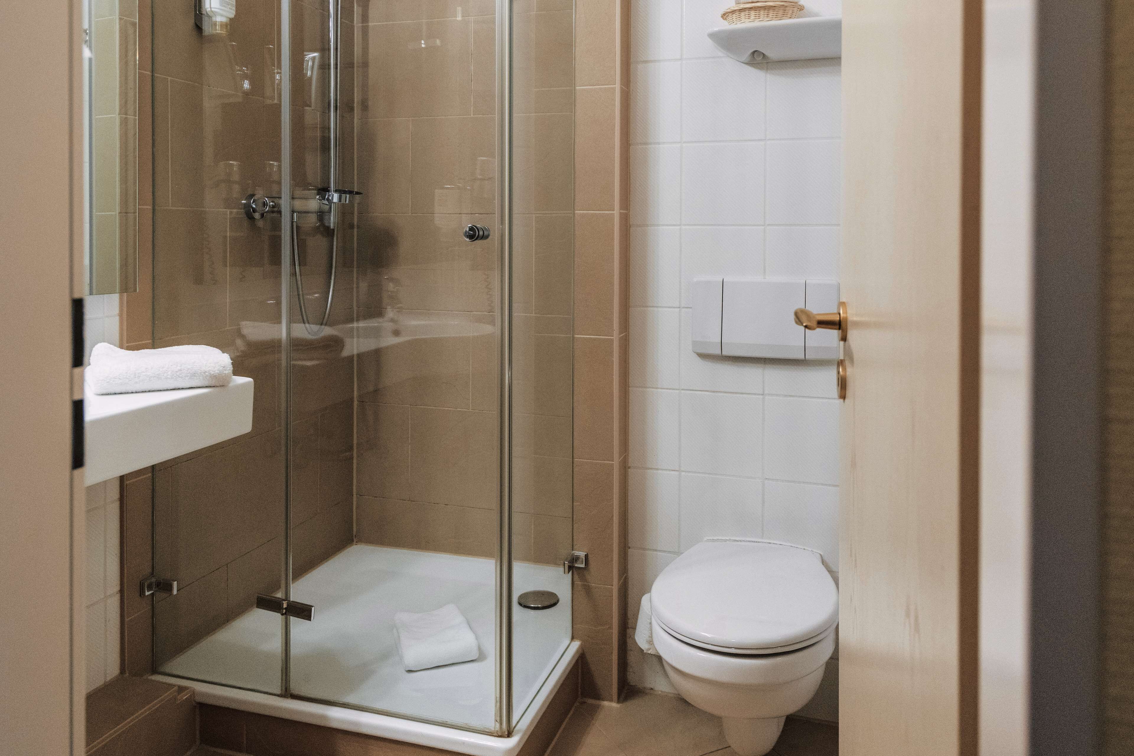A modern bathroom with a glass-enclosed shower, a white toilet, and a small shelf with a basket.