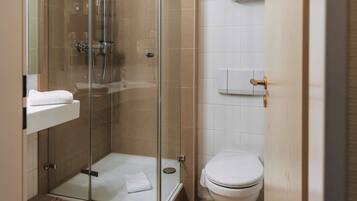 Ein modernes Badezimmer mit einer Duschkabine, einer weißen Toilette und einem kleinen Ablagebereich mit einem Korb.