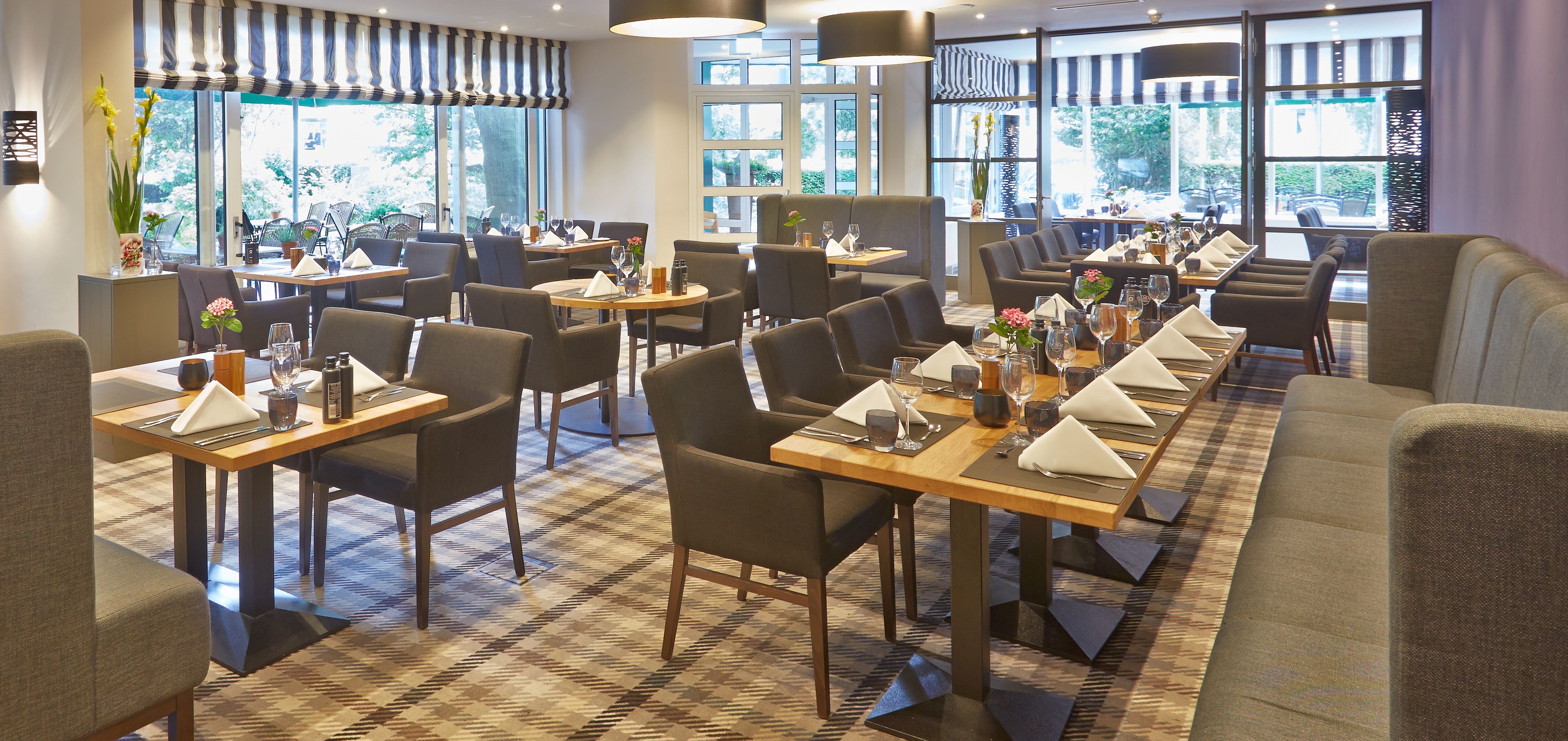Un restaurant doté de nombreuses tables et chaises, de grandes fenêtres et d’un tapis à motifs.