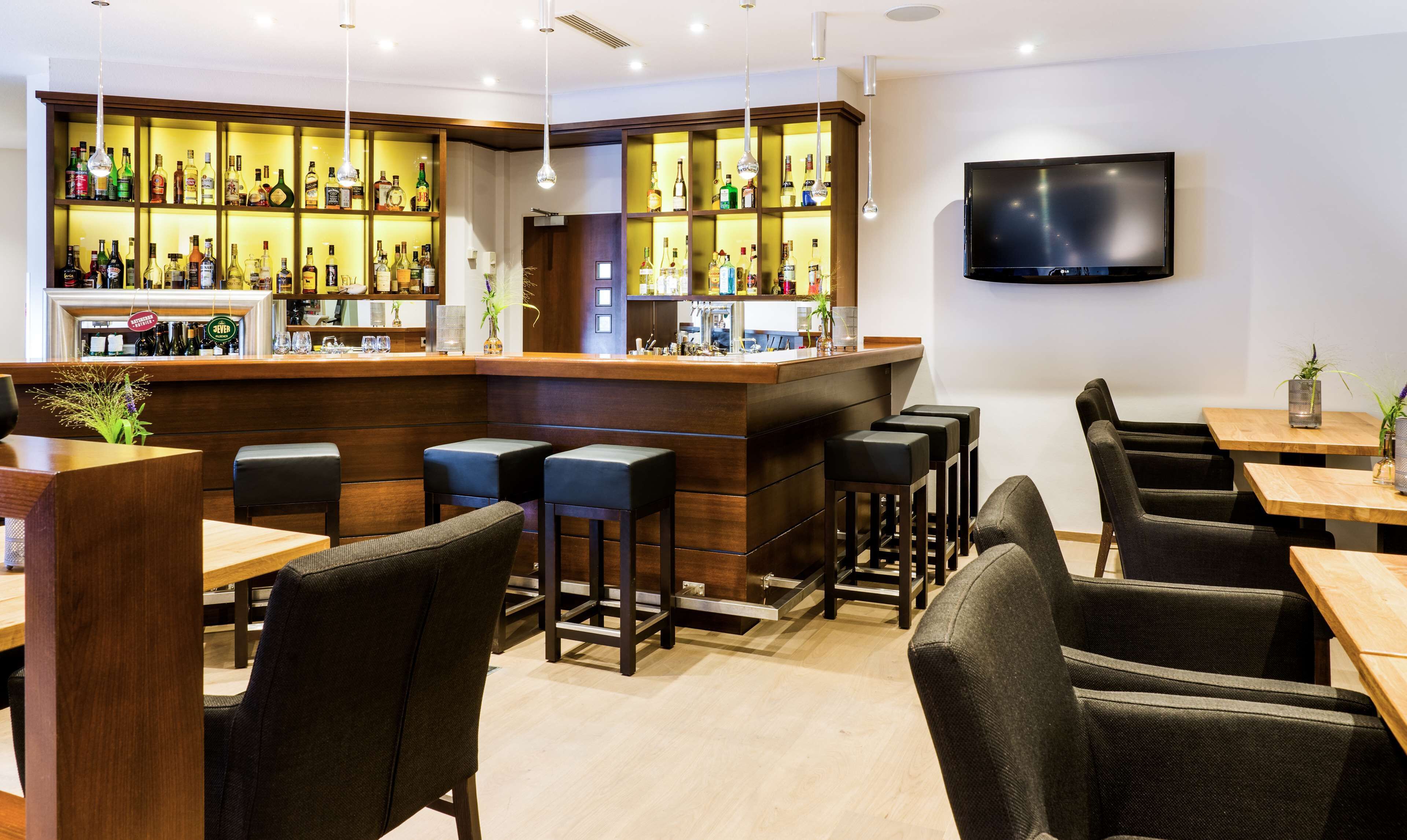 Eine Bar mit Holztresen, mehreren Hockern und einem an der Wand montierten Fernseher.