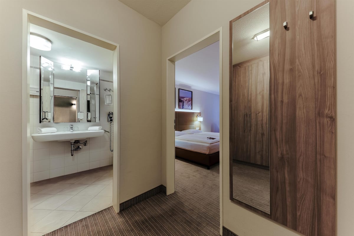 A hotel room with a bathroom, a bed, and a wooden wardrobe.