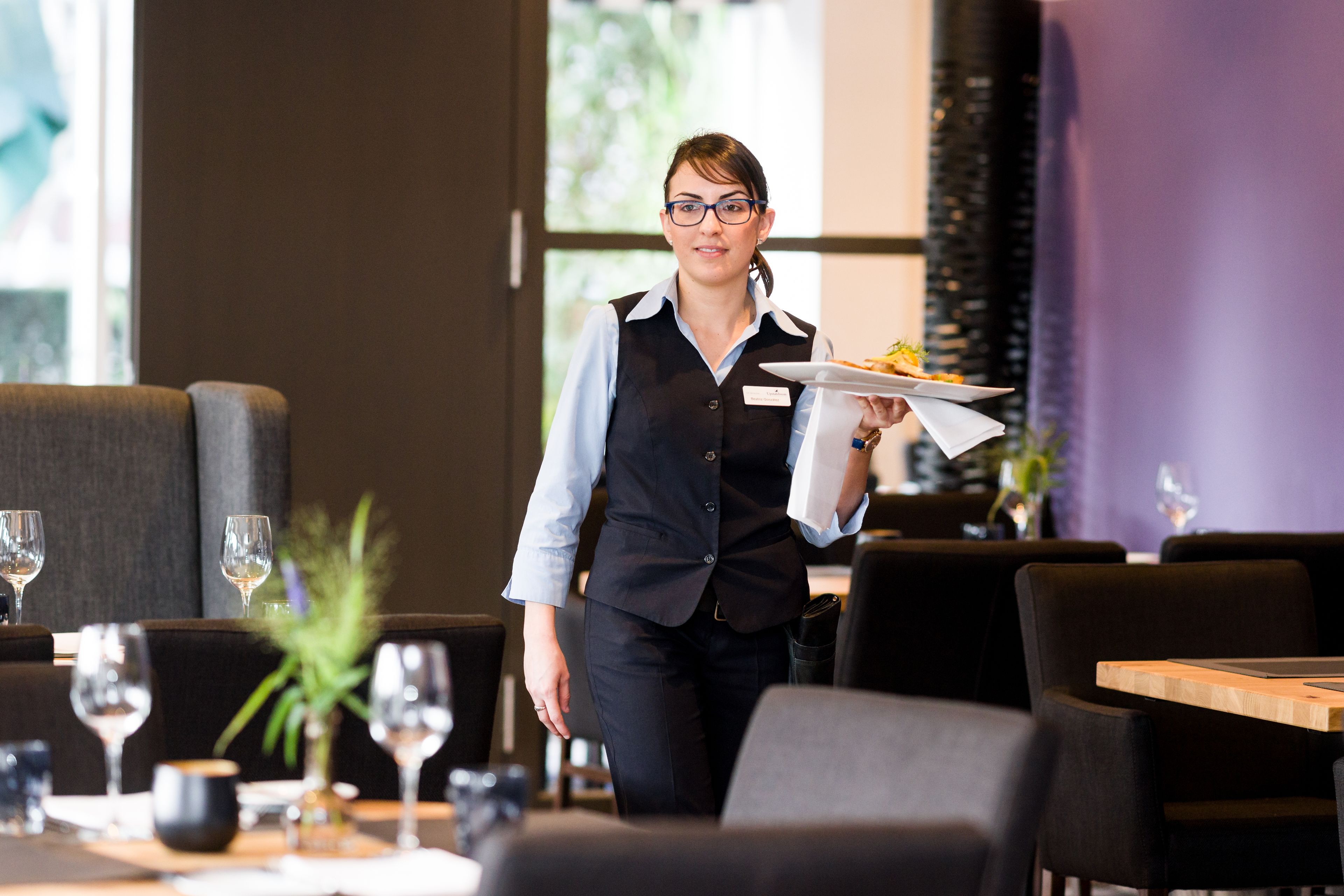 A waiter carrying a plate with food in a modern restaurant setting.