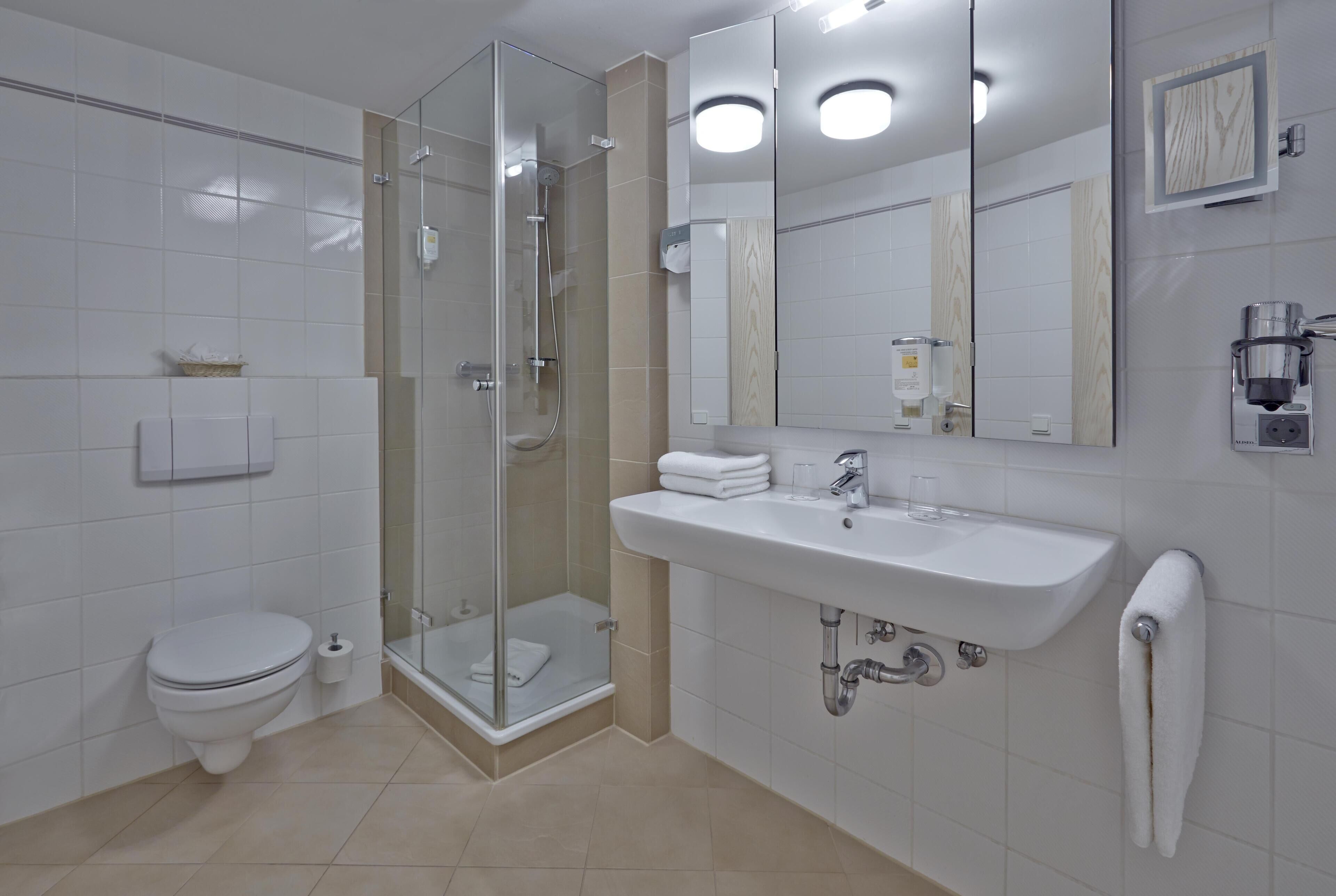 Un baño moderno con inodoro, cabina de ducha de vidrio, lavamanos y un perchero para toallas.