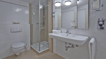 Un baño moderno con inodoro, cabina de ducha de vidrio, lavamanos y un perchero para toallas.