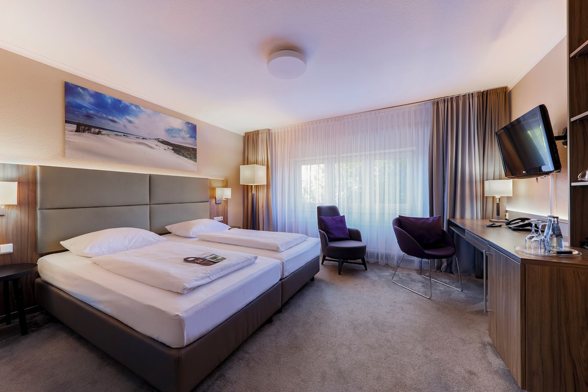 A hotel room with two beds, a desk, a chair, a television, and a painting on the wall.