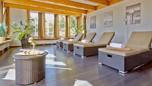 Un área de spa con sillones de mimbre, una chimenea pequeña y ventanas amplias con cortinas.