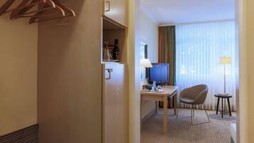 A hotel room with a wooden wardrobe, a desk with a chair, a television, and a lamp.