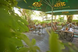 An outdoor dining area with wicker chairs and green umbrellas labeled "Jewel". - Upstalsboom Parkhotel (Emden)