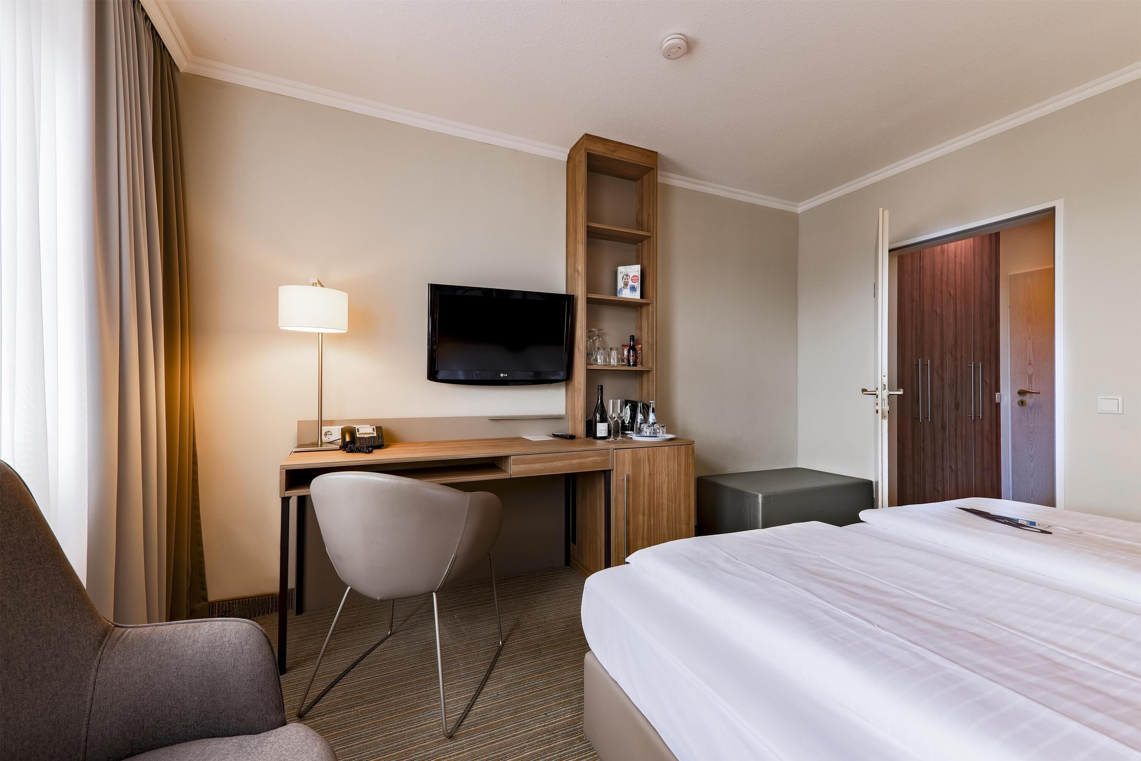 A hotel room with a bed, desk, chair, TV, and a wardrobe.