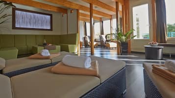 Ein Spa-Raum mit zwei Massagetischen, einem grünen Sofa und einem großen Fenster mit Vorhängen.