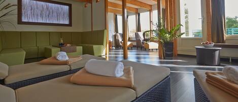 A spa room with two massage tables, a green sofa, and a large window with curtains.