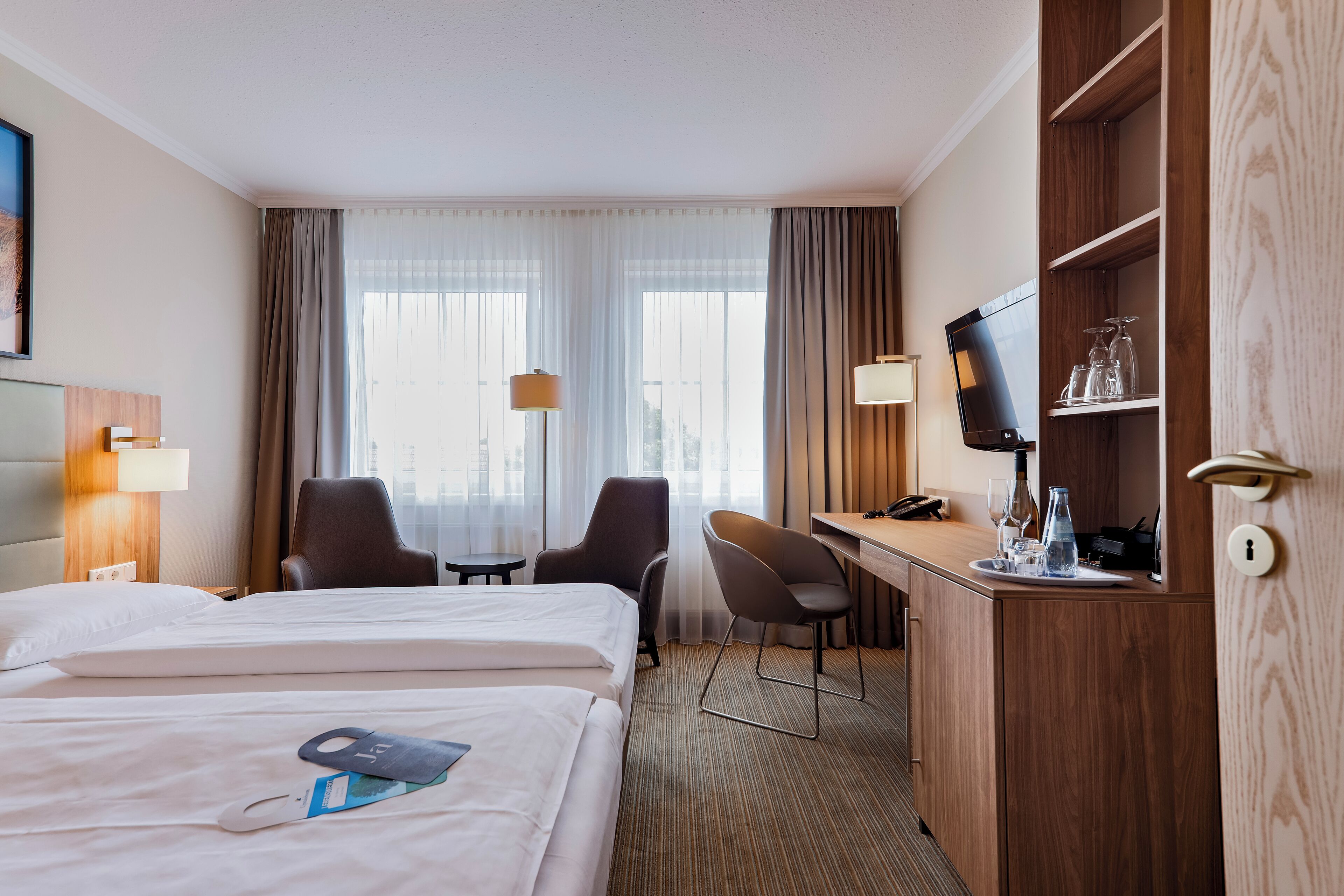 A hotel room with two beds, a desk, a chair, a TV, and a minibar.