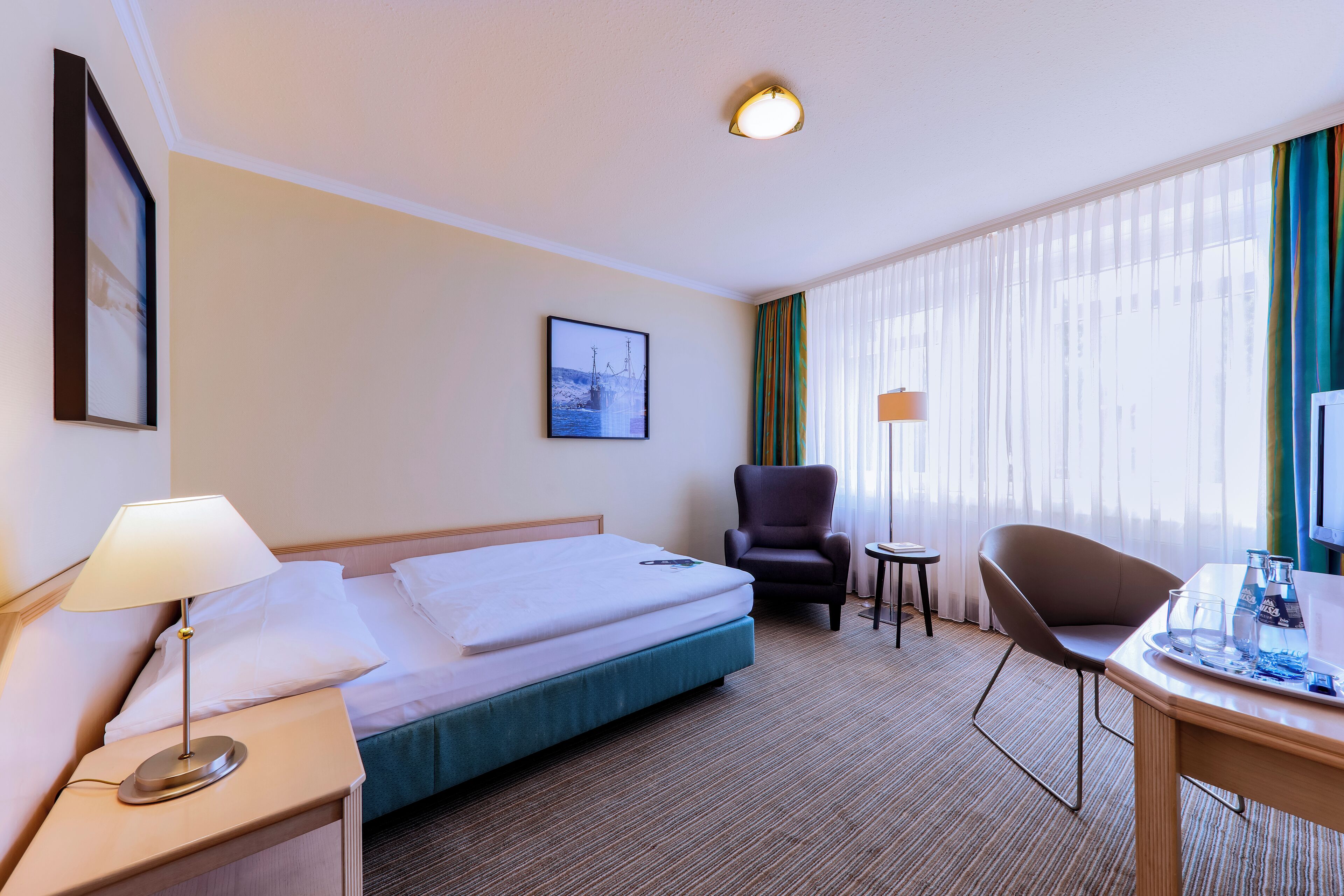 Een hotelkamer met een bed, een stoel, een bureau en een klein tafeltje.