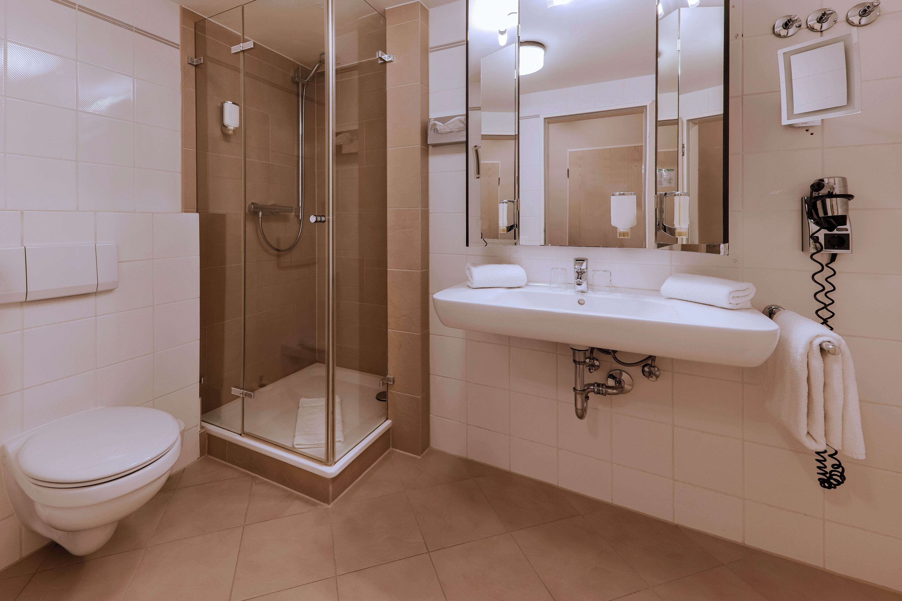 A modern bathroom with a toilet, glass shower enclosure, and a sink with a towel hanging on the wall.