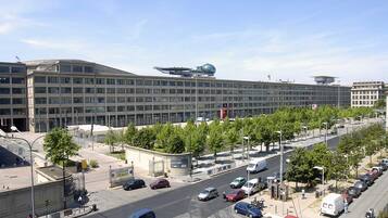 Ein modernes Gebäude mit flachem Dach, großen Fenstern und einem Parkplatz, auf dem Autos und Bäume stehen.