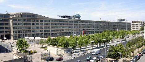 A modern building with a flat roof, large windows, and a parking lot with cars and trees.