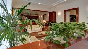 A spacious living room with a large sofa, a coffee table, and multiple potted plants.