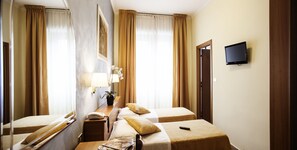 A hotel room with two beds, a bedside table with a lamp, a TV mounted on the wall, and a window with curtains. - Hotel Astor (Turin)