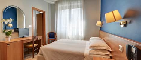 Quarto de hotel com cama, escrivaninha, cadeira, televisão, telefone e espelho.