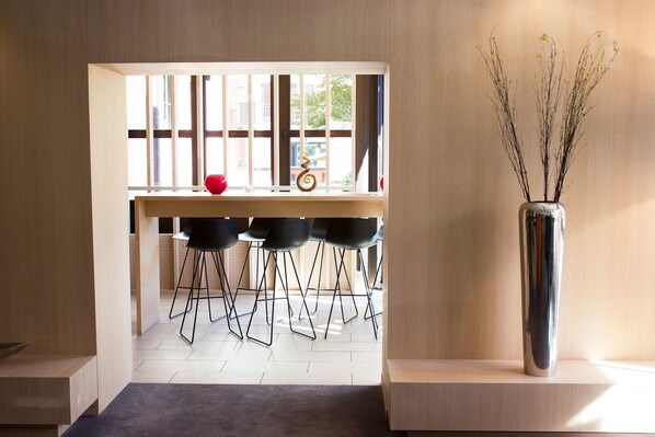 A modern interior with a wooden desk, black chairs, a red vase, and a tall vase with branches.