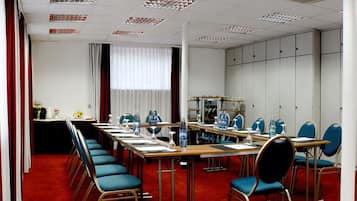 Een vergaderzaal met een lange tafel, blauwe stoelen en een rood tapijt.