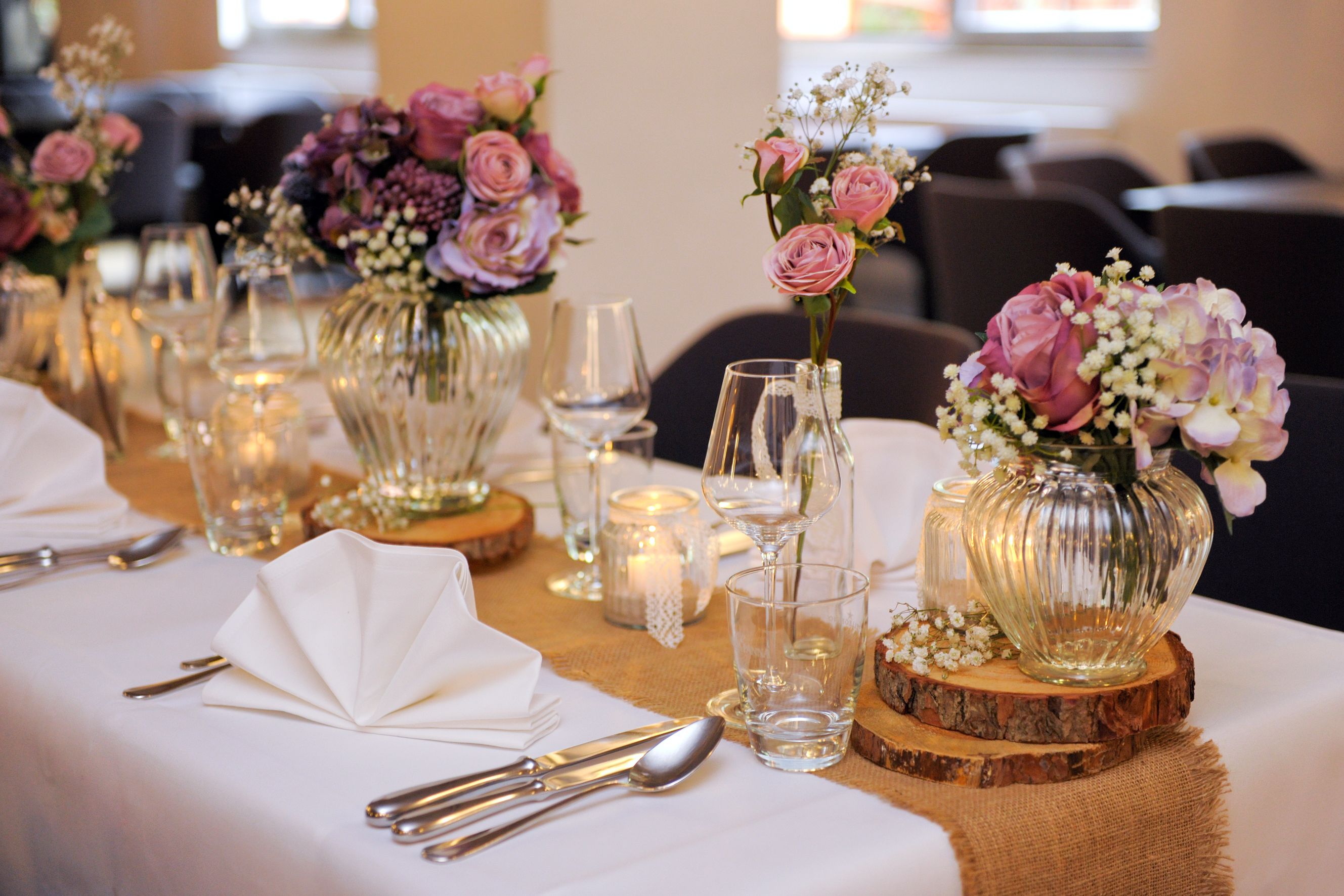 Et bord dækket til en formel lejlighed med glasvaser med blomster, stearinlys og bestik.