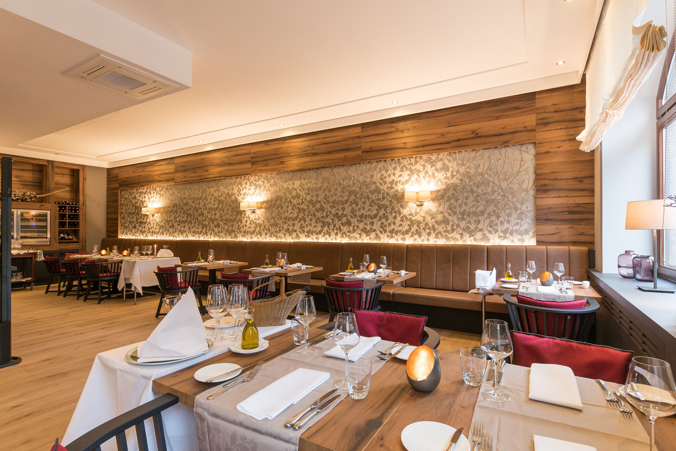 A restaurant with wooden paneling, tables set with white tablecloths, and red upholstered chairs.