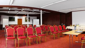 A conference room with rows of red chairs, a long table, and a whiteboard.