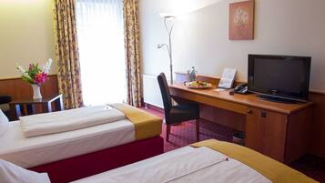 Habitación de hotel con dos camas, un escritorio con computadora y teléfono, una lámpara y un cuadro en la pared.