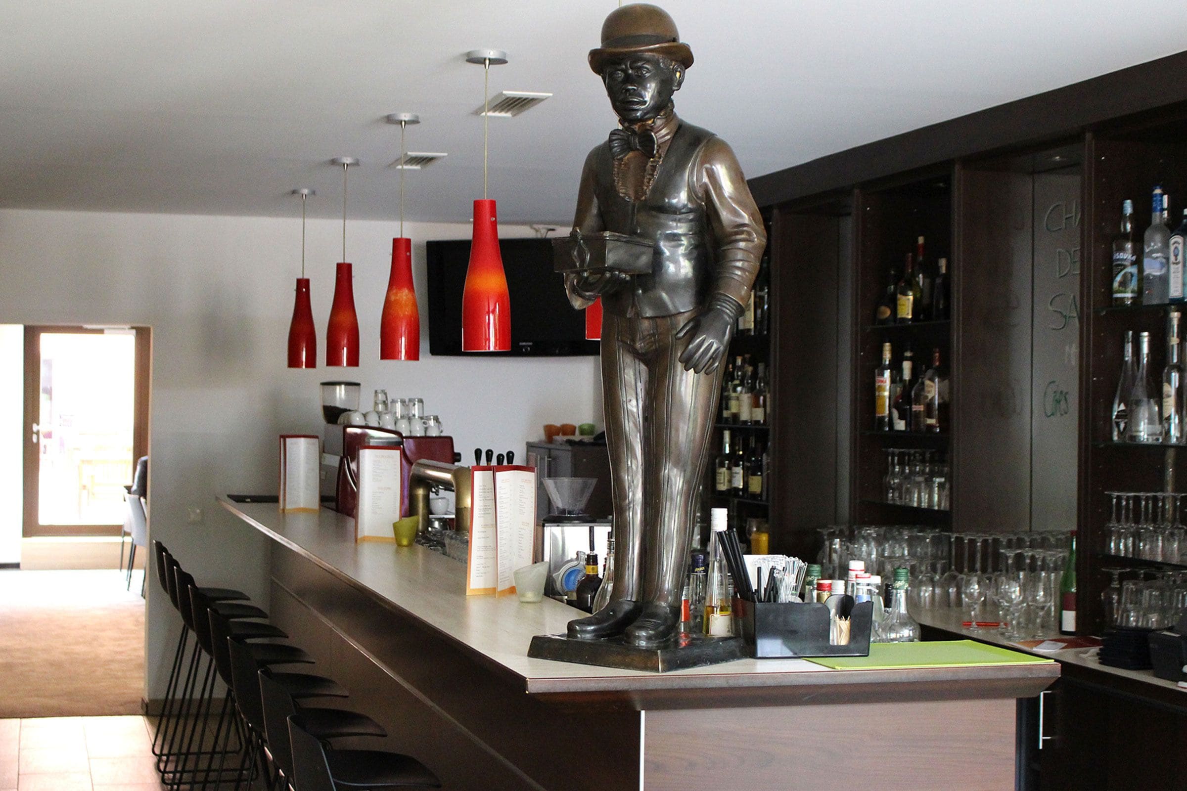 A bar area with a statue, bar stools, and various bottles and glasses.