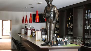 A bar area with a statue, bar stools, and various bottles and glasses.