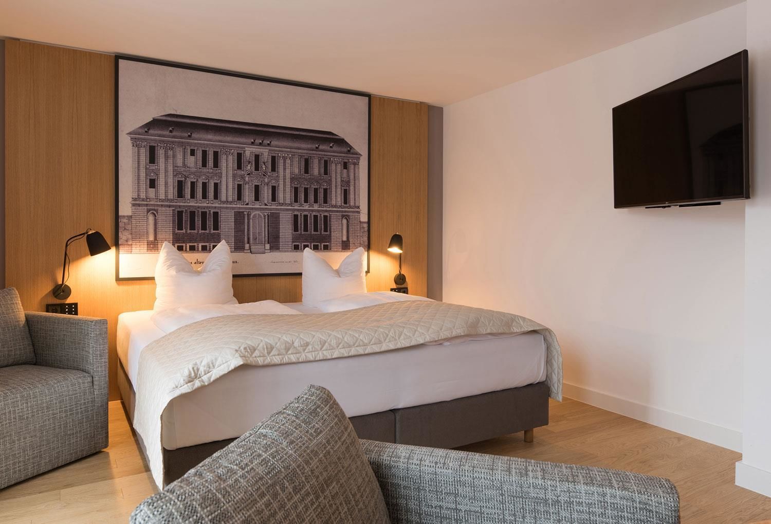 Habitación de hotel moderna con una cama grande, dos lámparas de noche, un televisor de pantalla plana y un dibujo arquitectónico enmarcado en la pared.