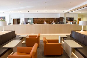 A modern hotel lobby with a reception desk, seating area, and a bookshelf.
