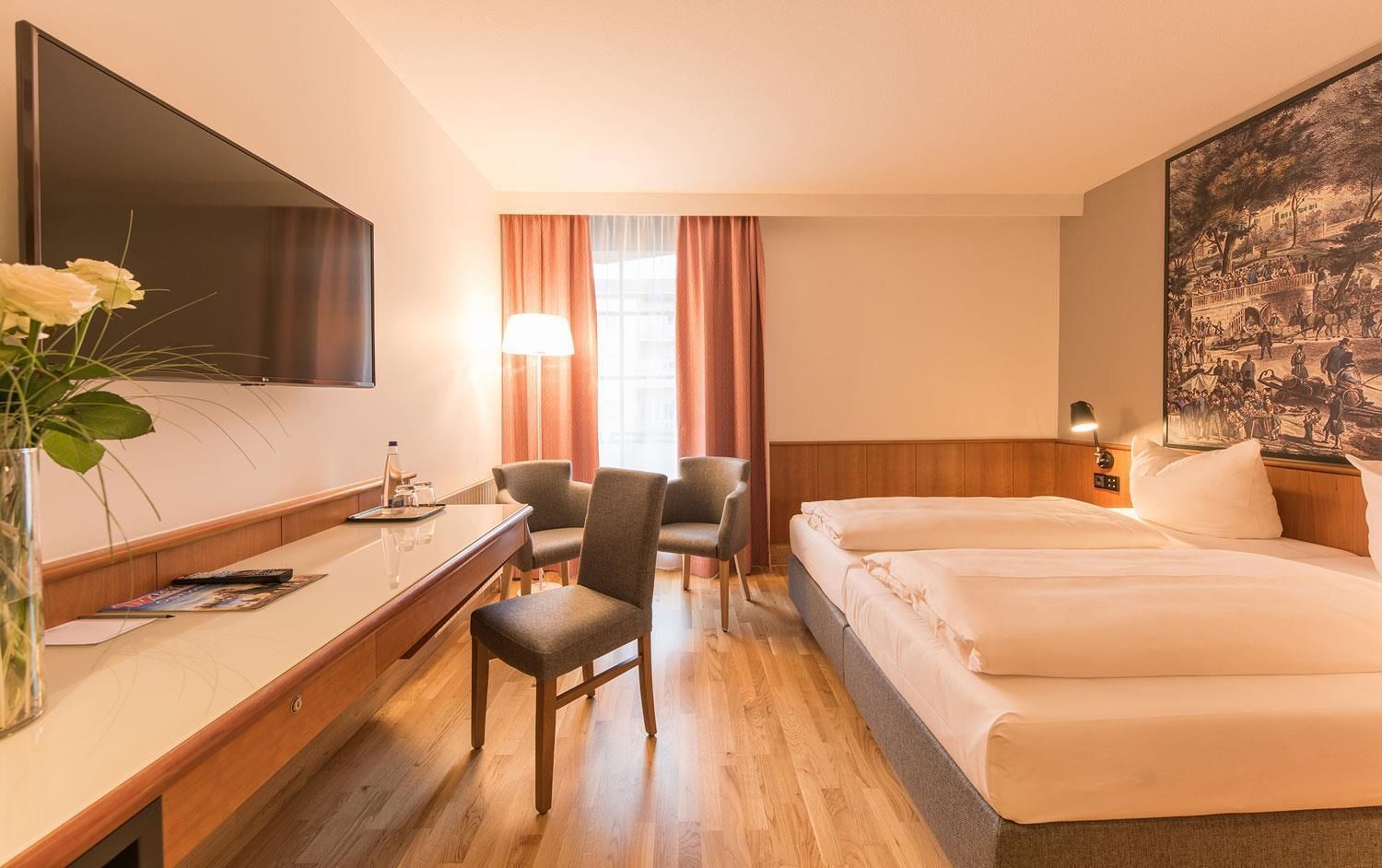 Een hotelkamer met een bed, een bureau, een stoel, een televisie en een schilderij aan de muur.
