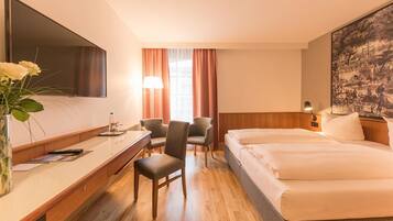 Een hotelkamer met een bed, een bureau, een stoel, een televisie en een schilderij aan de muur.