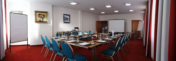 A conference room with a long table, blue chairs, a whiteboard, and a projector screen.