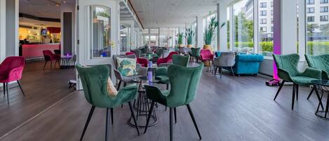 A spacious hotel lobby with modern furniture, a bar area, and large windows offering views of the city.