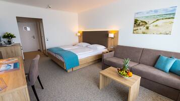 A hotel room with a bed, a sofa, a desk, and a painting of a beach scene.