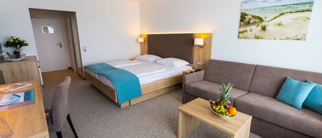 A hotel room with a bed, a sofa, a desk, and a painting of a beach scene.
